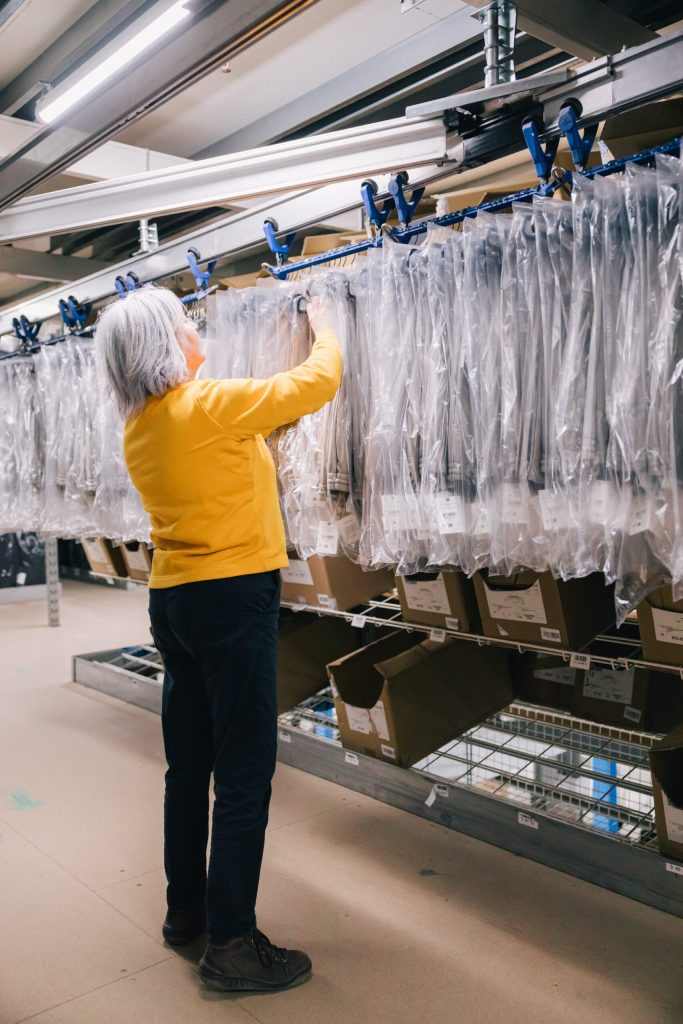 Femme travaillant chez C-LOG, prenant un vêtement sur un portant dans l'entrepôt dans le cadre de la logistique de la mode